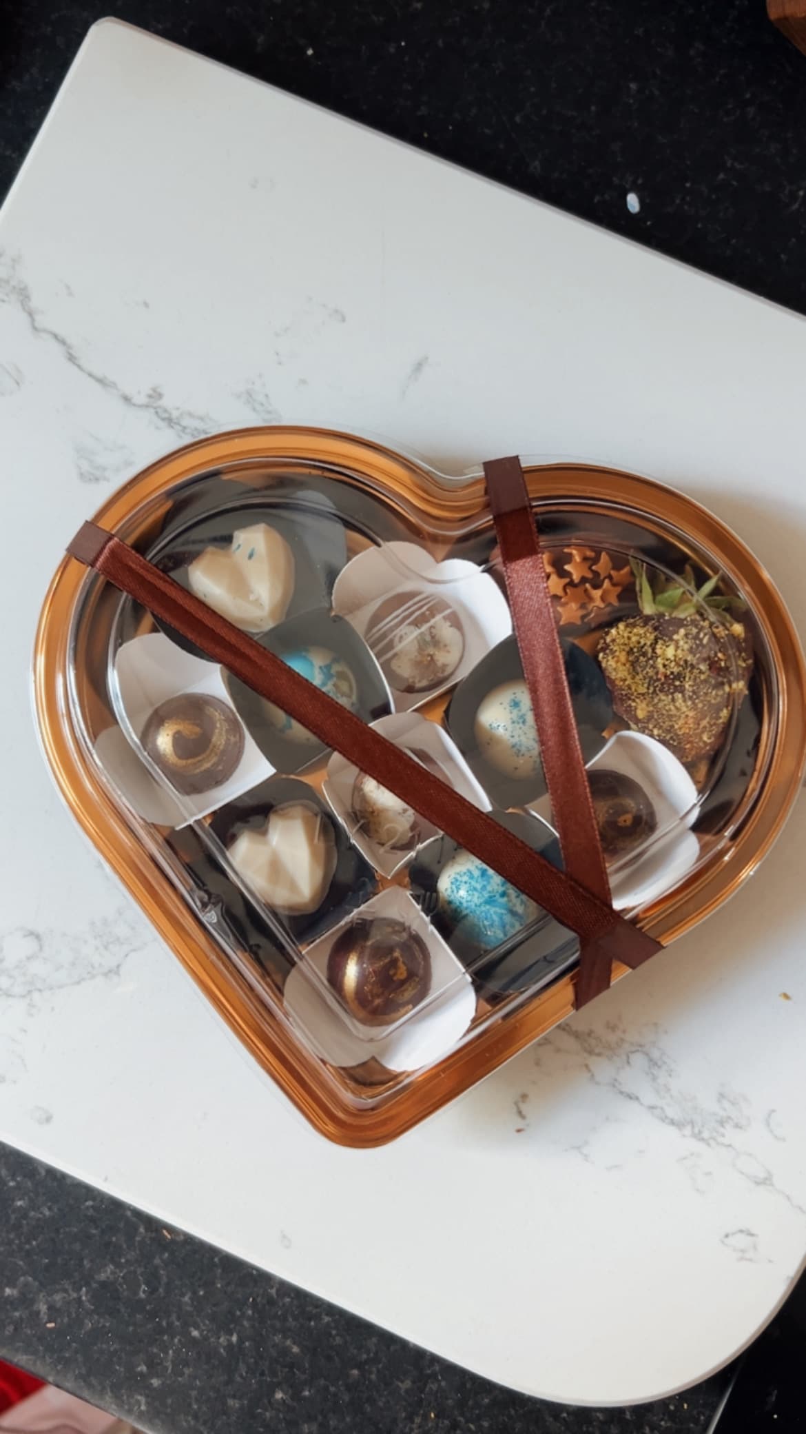 The signature heart box, ribbon-tied, over macro praline sections